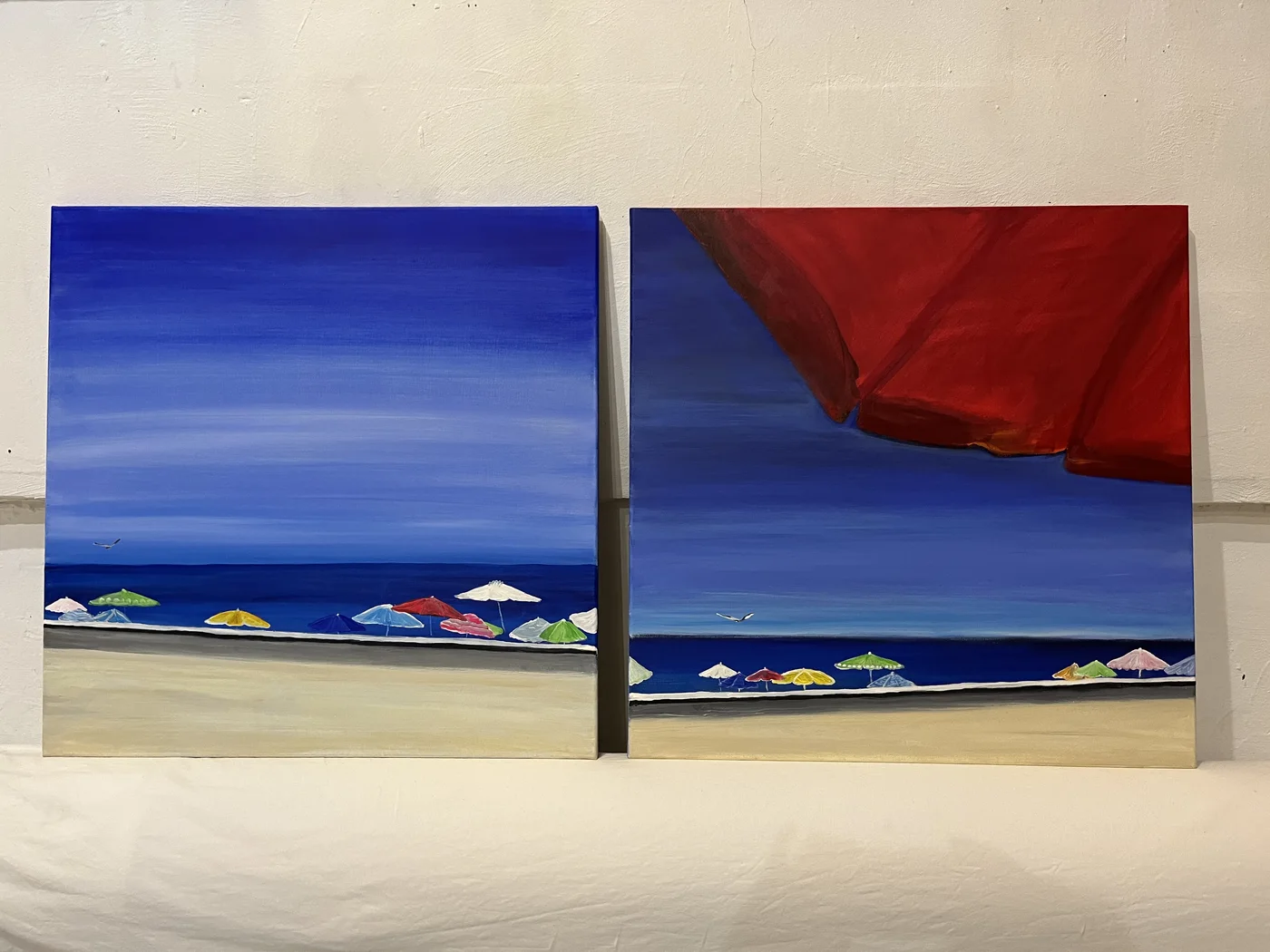 Zwei Strandgemälde mit bunten Sonnenschirmen, blauem Himmel und rotem Segel